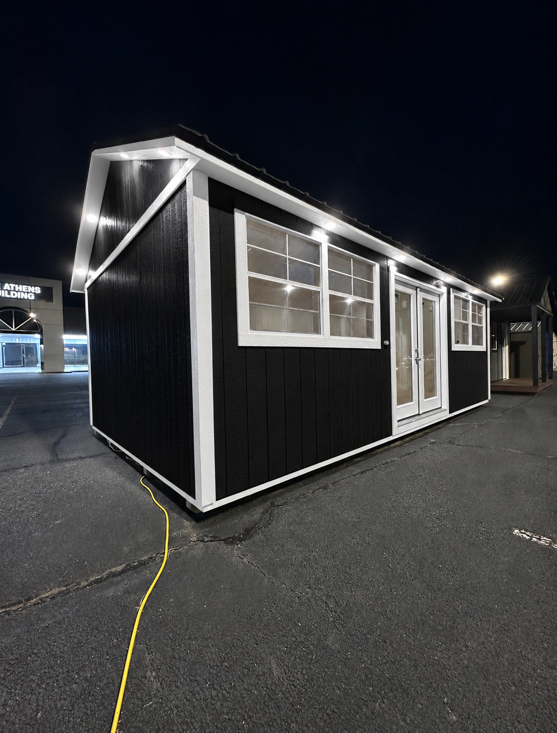 Modern black portable building with white trim lit at night under a dark sky